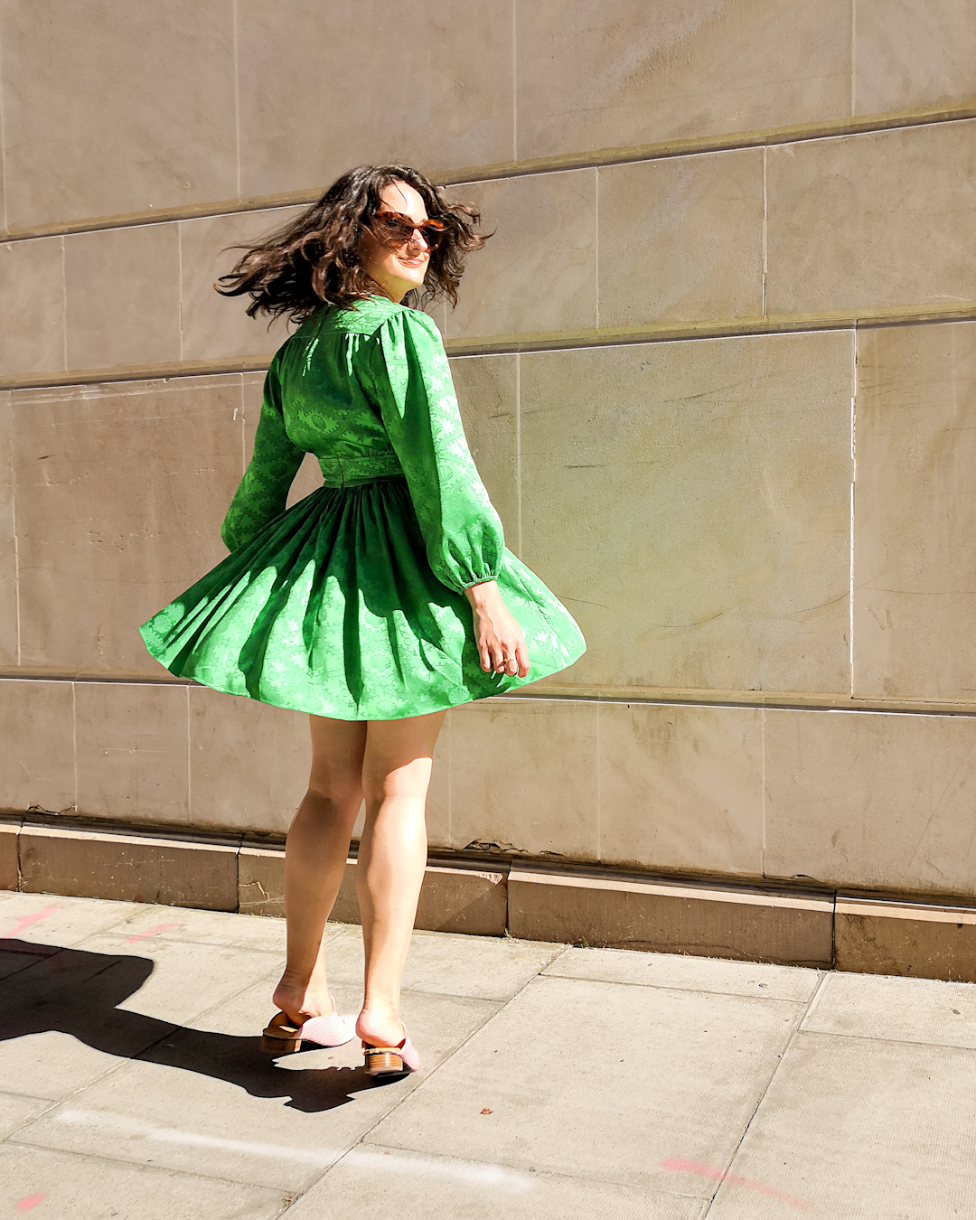 Katie wears a green dress with long poofy sleeves, a nipped in waist and short flouncy skirt. She's carrying a red shoulder bag and wearing pink slip on flats, and has accessorised with Berber style jewellery. In the first image she is twirling and her skirt is flared out.
